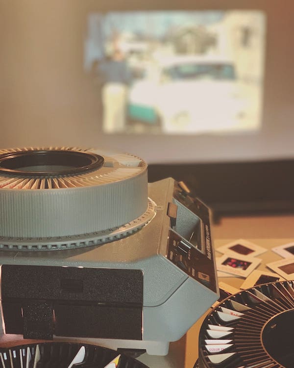 Close-up of a vintage slide projector with circular trays, projecting an image onto a blurred screen in the background.